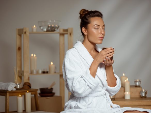 Young beautiful brunette girl holding tea cup relaxing in spa salon. Copy space.